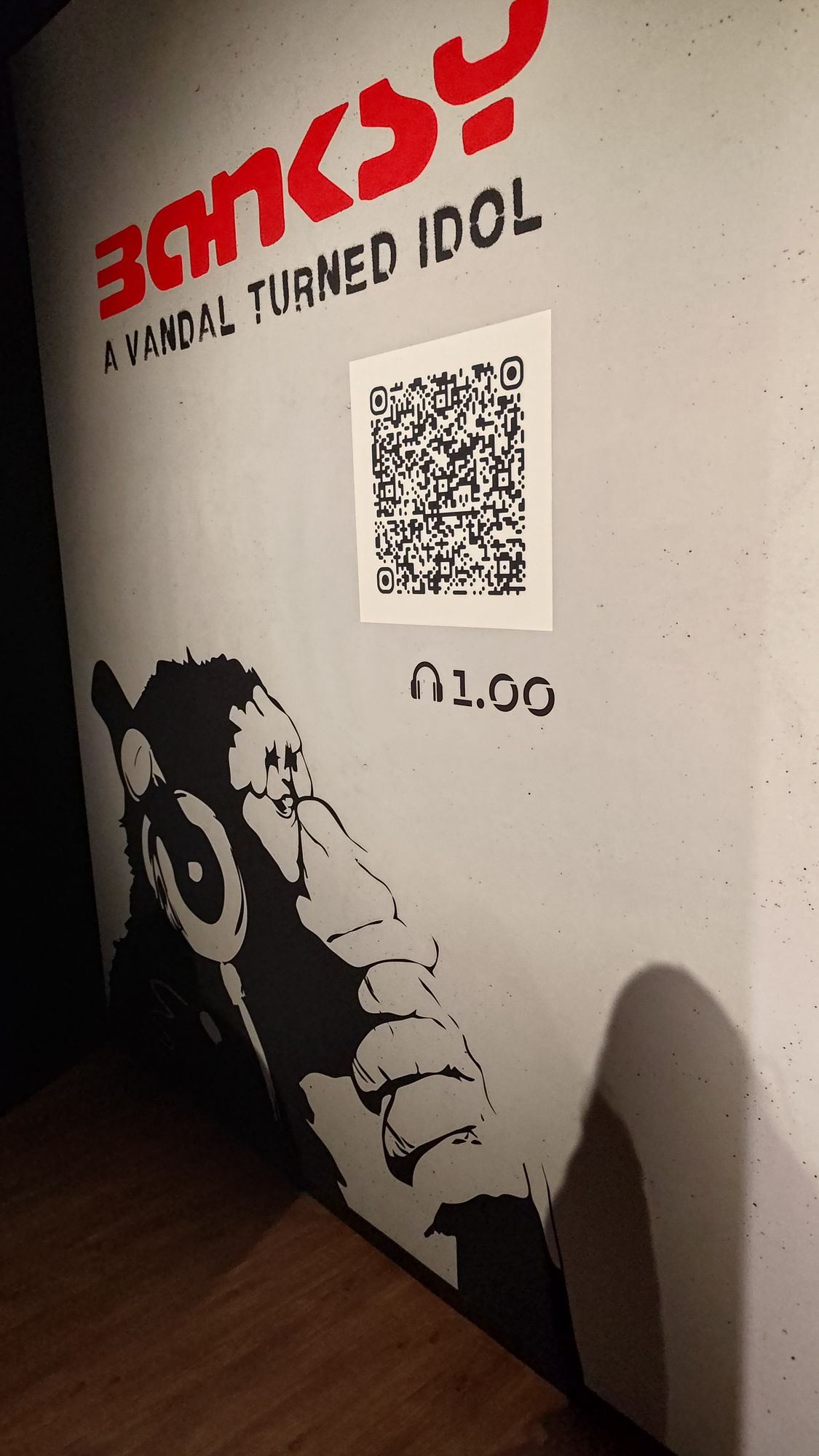 Der Ausstellungstitel am Eingang über einem Affen mit Kopfhörern, daneben ein QR-Code