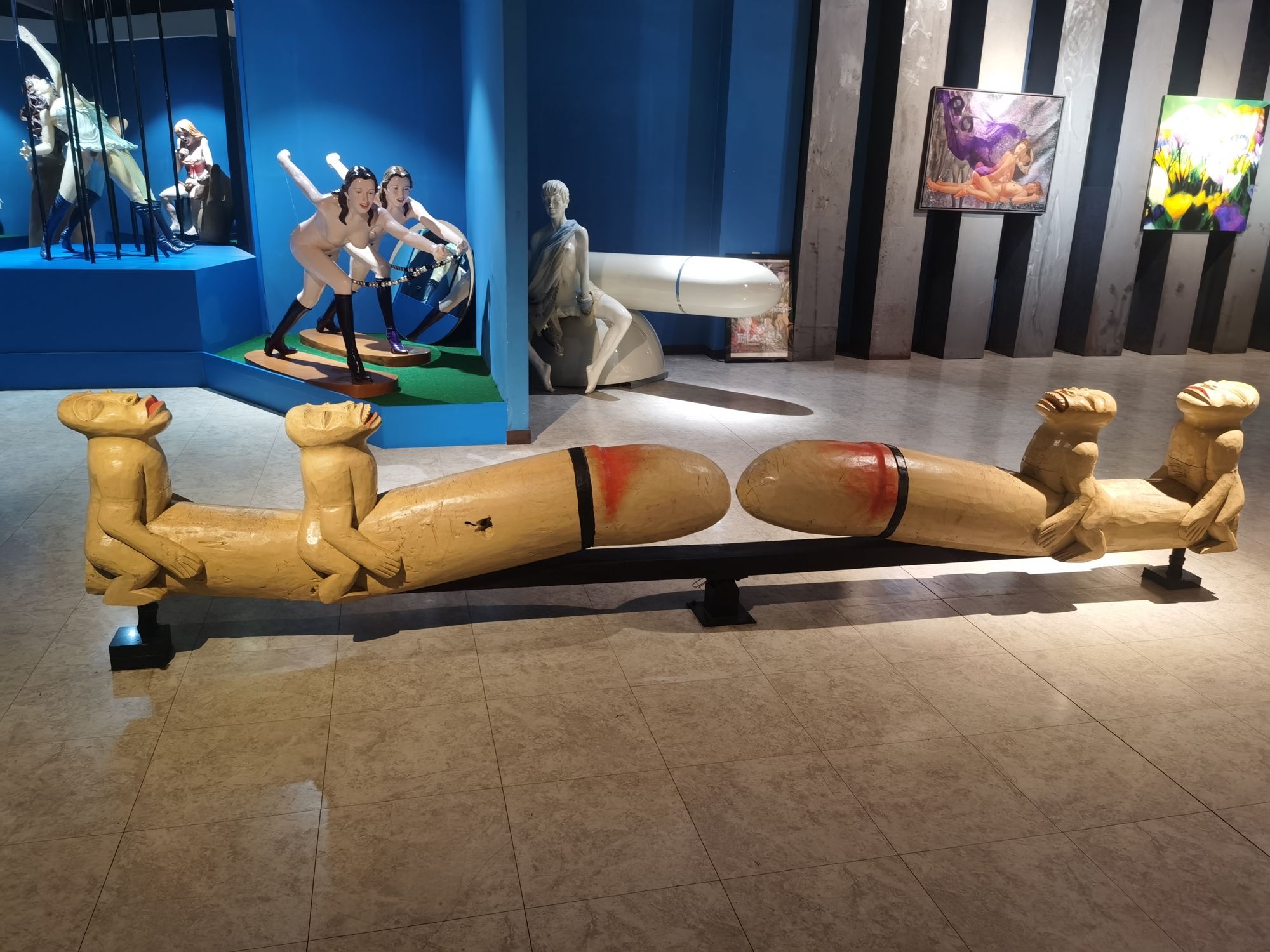 A wooden bench made of two reclining phalluses, with figure scenes behind