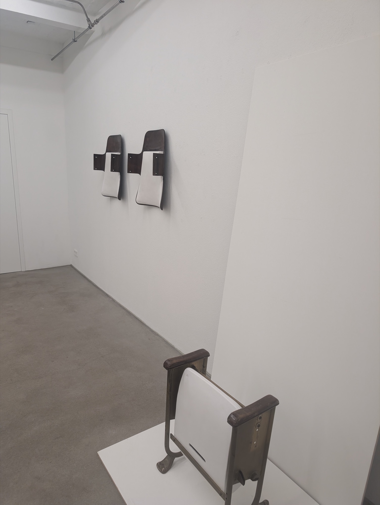 Zwei Sitzschalen an der Wand, vorn ein alter Klappsitz auf weißem Sockel, Konrad Fischer Galerie