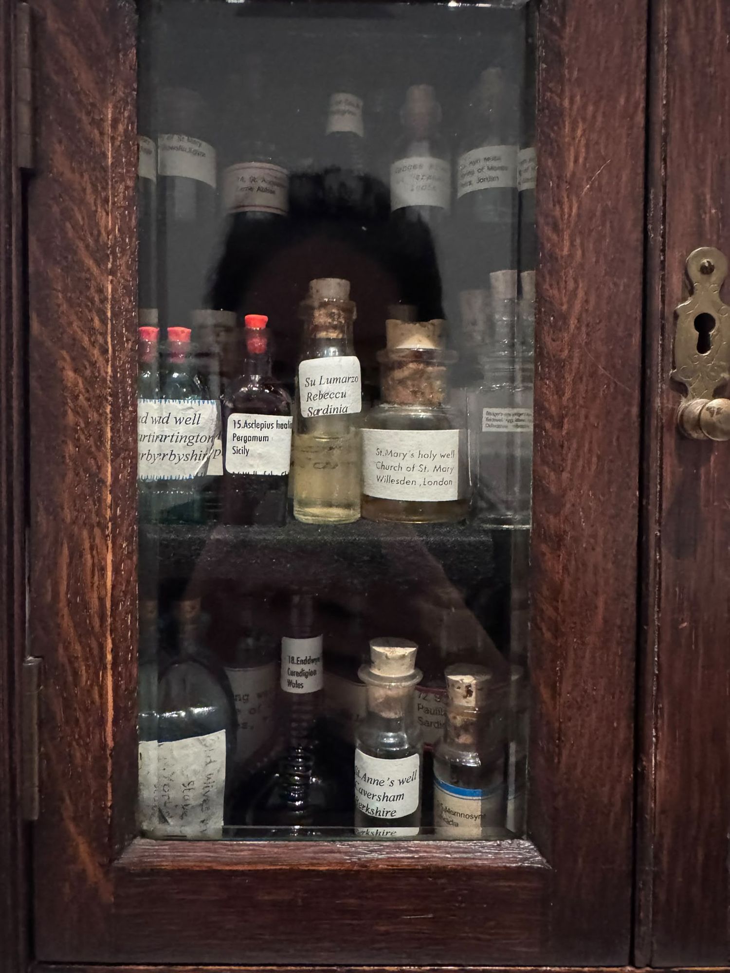 Susan Hiller, „Homage to Joseph Beuys“, seit 1969, Flaschen mit Wasser aus heiligen Quellen in einem Holzschrank, darunter St. Mary's holy well in Willesden und St. Anne's well in Caversham