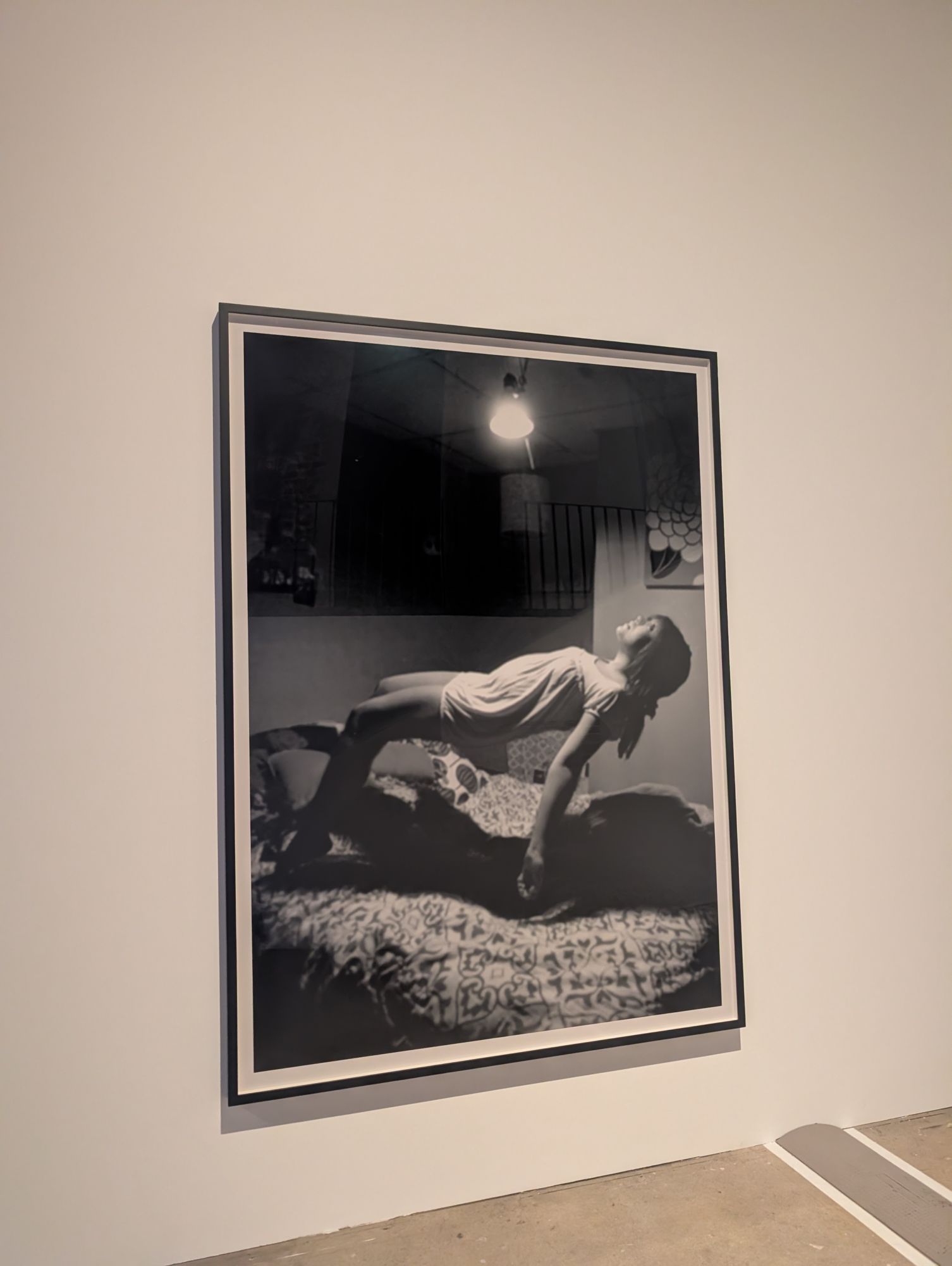Susan Hiller, aus „Levitations (Homage to Yves Klein)“, ein Mädchen schwebt waagerecht über einem Bett unter einer nackten Glühbirne
